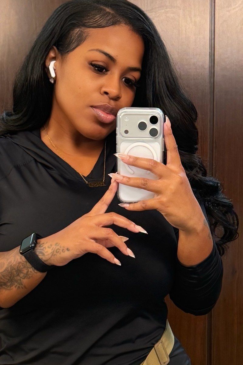 After photo of @jasminbadd, a mirror selfie in a locker room in a black long sleeved top with a camouflage belt bag.